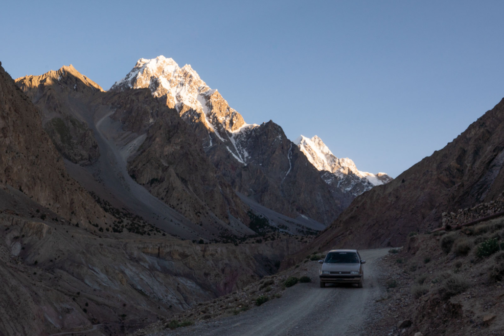 car coming down red sand road with mountains in background